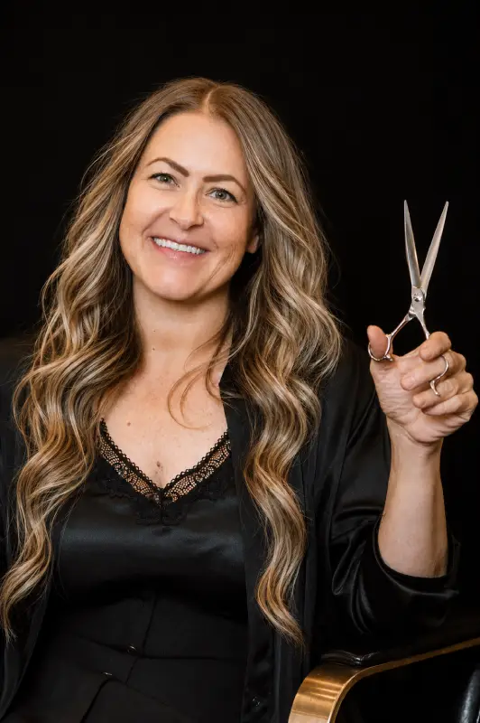 Smiling woman with long hair holding hairdressing scissors.
